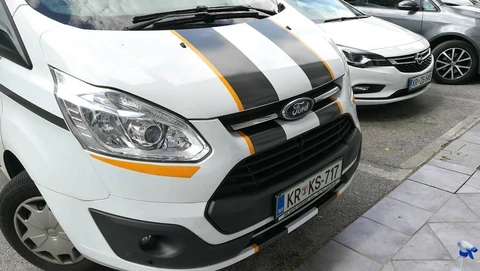 Črno-oranžni pasovi na pokrovu belega kombija